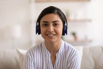 Head shot portrait smiling Indian woman in headphones chatting online with friends, sitting on...