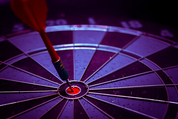 Close up shot of the dart arrow hit on bulleyes of dartboard to represent that the business reached the target of company with dark tone picture style. Target and goal as concept.