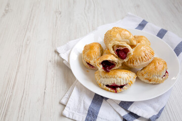 Homemade Cherry Hand Pies on a plate on a white wooden background, side view. Copy space.