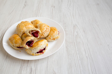 Homemade Cherry Hand Pies on a plate on a white wooden background, side view. Copy space.