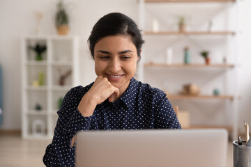 Close up smiling Indian woman looking at laptop screen, positive successful businesswoman freelancer working online at home, happy millennial female watching video, chatting in social network