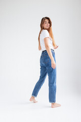 young attractive caucasian woman with long hair in t-shirt and blue jeans isolated on white studio background. skinny pretty female posing on cyclorama with bare feet. model tests of beautiful lady