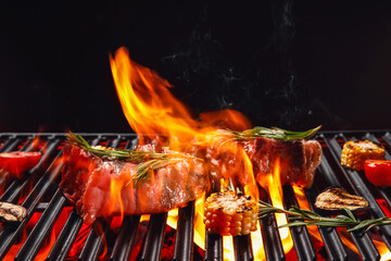 Barbecue grill with steaks, rosemary and vegetables on dark background