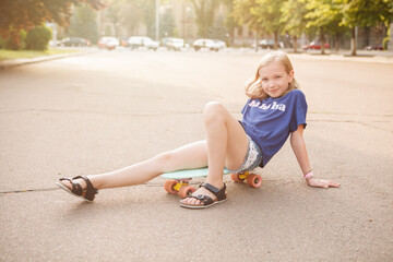 Adorable young girl smiling to the camera, sitting on her pennyboard in the city
