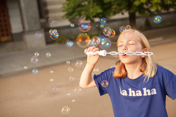 Young girl blowing soap bubbles outdoors, copy space