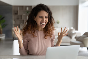 Overjoyed millennial Latino woman look at laptop screen feel euphoric read good news online....