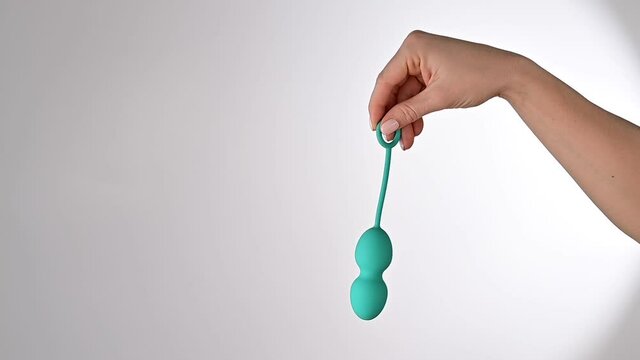 Faceless woman demonstrates a turquoise vaginal ball. Girl holding a kegel trainer for training pelvic floor muscles on a white background.