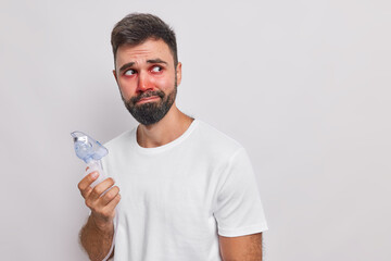 Bearded young man uses medical equipment for inhalation has asthmatic attack allergic reaction red...