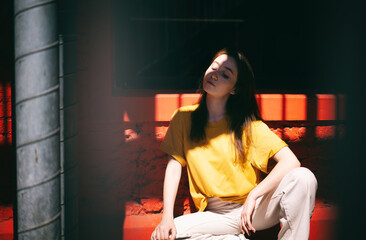 Obraz na płótnie Canvas Portrait of a young happy trendy modern brunette woman in a yellow t-shirt on a background of red shadow with shadow in face