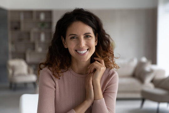 Portrait of happy millennial Hispanic female tenant or renter sit pose in modern renovated home or apartment alone. Smiling young Latino woman laugh feel optimistic relax rest. Diversity concept.