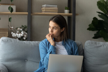 Pensive woman sit on sofa with laptop. Female student use internet resources e-learning, thinks...