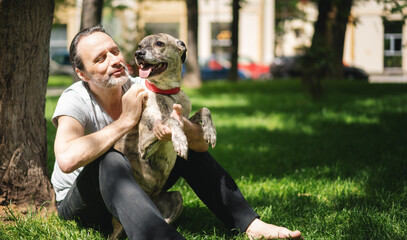 Happy attractive mature man 50 years old resting on the grass while walking with his dog in his arms