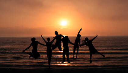 Silhouettes Of Happy Young People Jumping On the Sunset Beach. Boys and Girls  Enjoying life Together. Holidays, Happiness and youth concept 