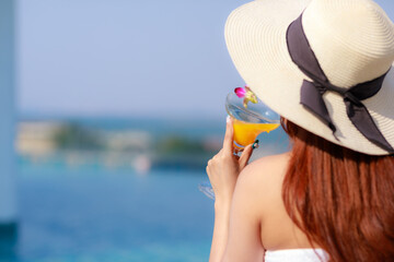 Portrait of a beautiful woman relaxing with orange juice at the swimming pool outdoors. holiday and vacation concept.