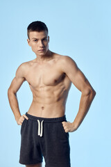 Fototapeta premium athlete in shorts holds his hands on the belt on a blue background inflated torso muscles of a bodybuilder