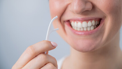 Close-up portrait of a beautiful caucasian woman with a flawless smile holding a toothpick with dental floss on a white background