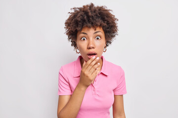 Fototapeta na wymiar Portrait of surprised Afro American woman gasps from wonder stares speechless in awe and disbelief cannot believe her eyes wears casual t shirt isolated over white background. Human reaction