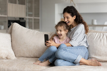 Overjoyed young Hispanic mother and teen daughter use smartphone triumph read good news online. Smiling Latino mom and teenage girl child feel euphoric win online lottery on cellphone. Luck concept.