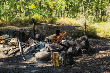 Summer camping with campfire and axe in a tree stump. Cooking food in forest on wooden firewood. Axe ready for cutting timber on summer picnic and making bonfire. Survival in wild nature concept.