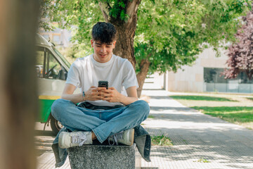 Obraz premium male teenager sitting on the street with mobile phone