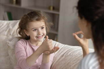 Obraz na płótnie Canvas Small ethnic girl child make hand gesture talk with mom use sign language. Smiling little biracial numb deaf disabled kid communicate with tutor or coach. Disability, nonverbal communication concept.