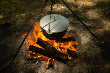 Tourists prepare lunch in hiking pot on campfire at campsite. Bowler on bonfire. Soup boils in cauldron.