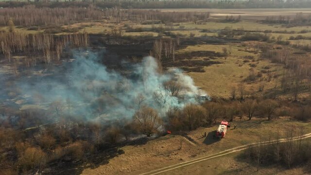 Aerial View. Spring Dry Grass Burns During Drought Hot Weather. Bush Fire And Smoke. Fire Engine, Fire Truck On Firefighting Operation. Wild Open Fire Destroys Grass. Ecological Problem Air Pollution