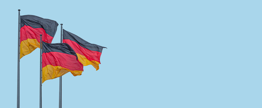 Banner with three national black red yellow flags of Germany in wind and at blue sky background with copy space, details, closeup. Concept of nationality, citizenship and patriotism.
