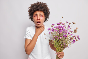 Curly Afro American woman suffocates has allergic reaction on wildflowers keeps hand on throat has...