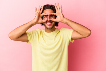 Young caucasian man isolated on pink bakcground showing okay sign over eyes