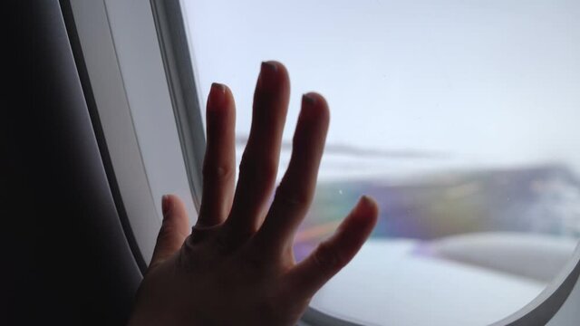 Close up woman passenger on window seat hand touch on airplane window inside the cabin with snowy outside runway, snowing airport, travelling on winter,  cold and lonely feeling, missing out and sad