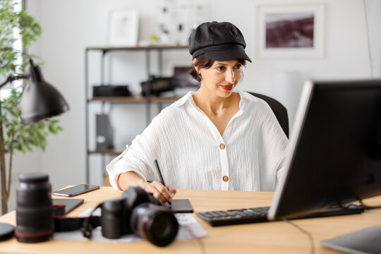 Attractive woman in stylish wear retouching photos at modern office. Female photographer using computer and stylus pen for work.