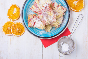Strawberry souffle cake on blue plate and wheels of dried orange, eggshells on white wooden desk, view from the top.