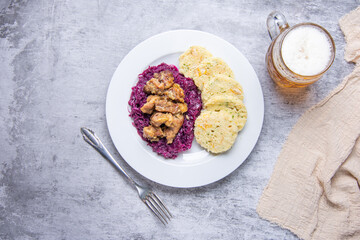 Roast pork with dumplings and sauerkraut. Typical Czech national dish with homemade bread dumplings red cabbage and beer on concrete background. Top view.
