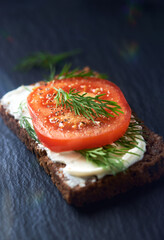 Tomato sandwich with cream cheese on dark stone background. Close up. 