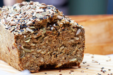 Buckwheat gluten-free bread with a brown crust, sprinkled with seeds, lies on a wooden table. A healthy homemade recipe. Grains of green buckwheat are scattered nearby. View from above.
