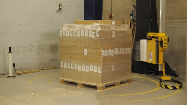 Machine wraps plastic around pallet with cardboard boxes in a factory