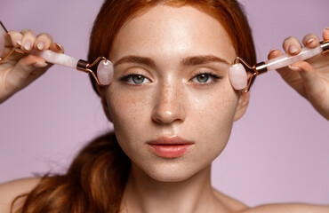 Close up of redhead girl, with clean perfect skin, using skincare massage jade rollers, cosmetic...