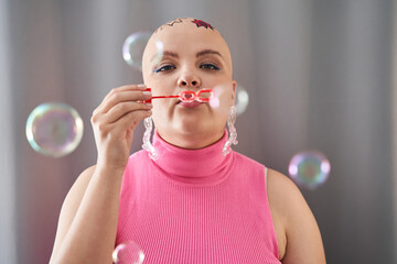 Bald girl blowing soap blebs with enjoyment while spending time at home