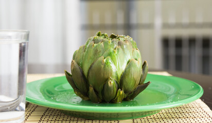 cooked whole artichoke on a green plate