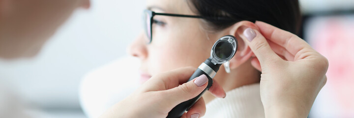 Otorhinolaryngologist examines patient ear with an otoscope - obrazy, fototapety, plakaty