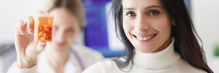 Smiling female patient holding pills in background of doctor