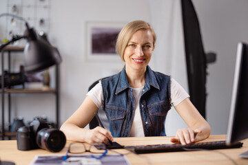 Front view of pleasant woman in casual clothes retouching photos on bright office. Female photographer using modern computer and stylus pen for work.