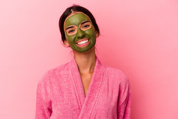 Young caucasian woman wearing a bathrobe and facial mask isolated on pink background happy, smiling and cheerful.