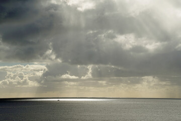 Obraz premium Bright sunlight breaks through the open ocean clouds. Atlantic. Glare on the surface of the water