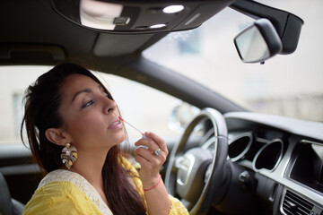 Fototapeta na wymiar Latin woman in yellow dress painting her lips inside a car.