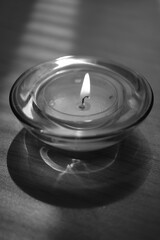 Obraz na płótnie Canvas Low candle burns in a round glass candlestick on the dark table. BW photo