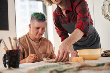 Sculptor standing near the table with boy with special needs and explaining to him