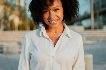 A close-up portrait of an Afro-looking woman looks into the camera and smiles. The clothing is a classic white shirt.