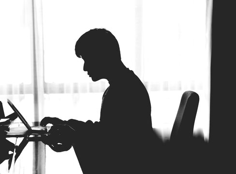 A silhouette of a man sitting at his desk in the office by the window.